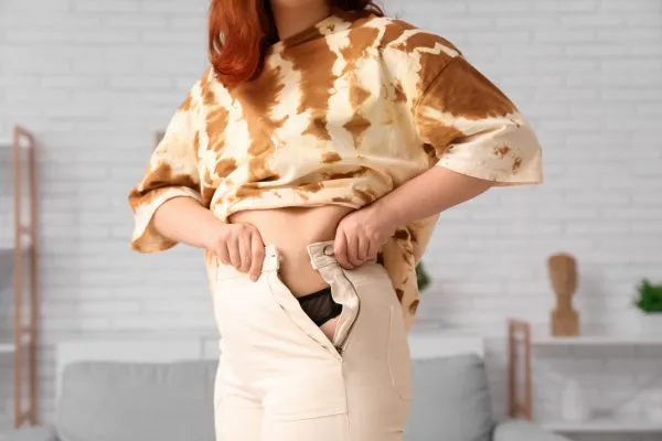 Image of woman trying to do her trousers up after pregnancy weight gain Bury