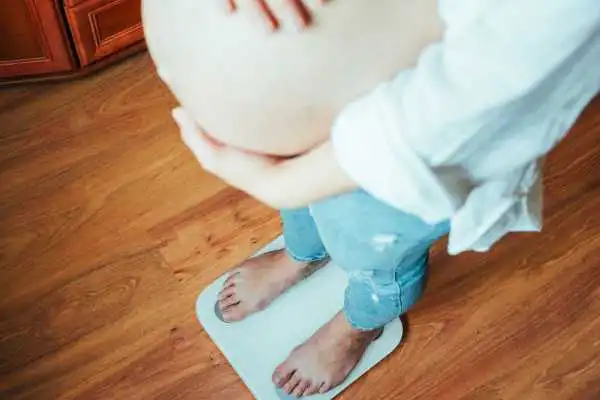 Image of woman weighing herself and experiencing weight gain through pregnancy Bury